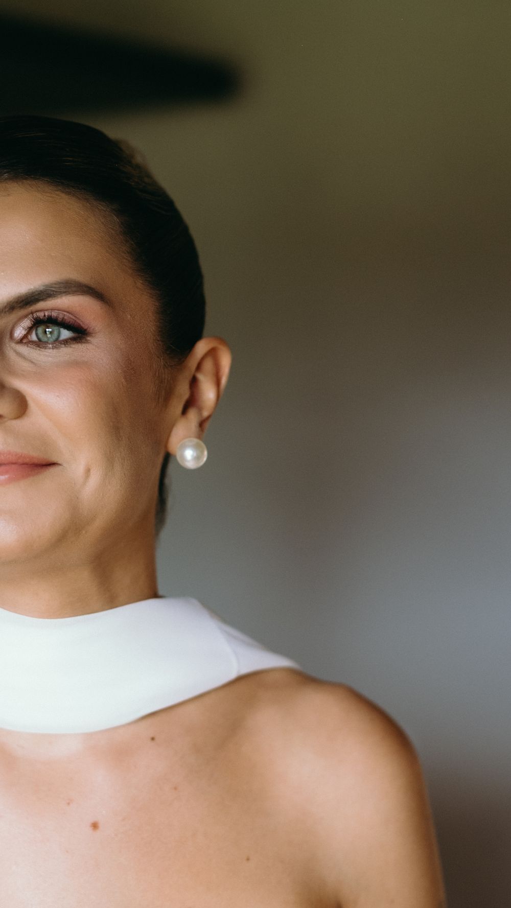 Bride wearing pearl earring and white halter neckline smiling softly on wedding day.