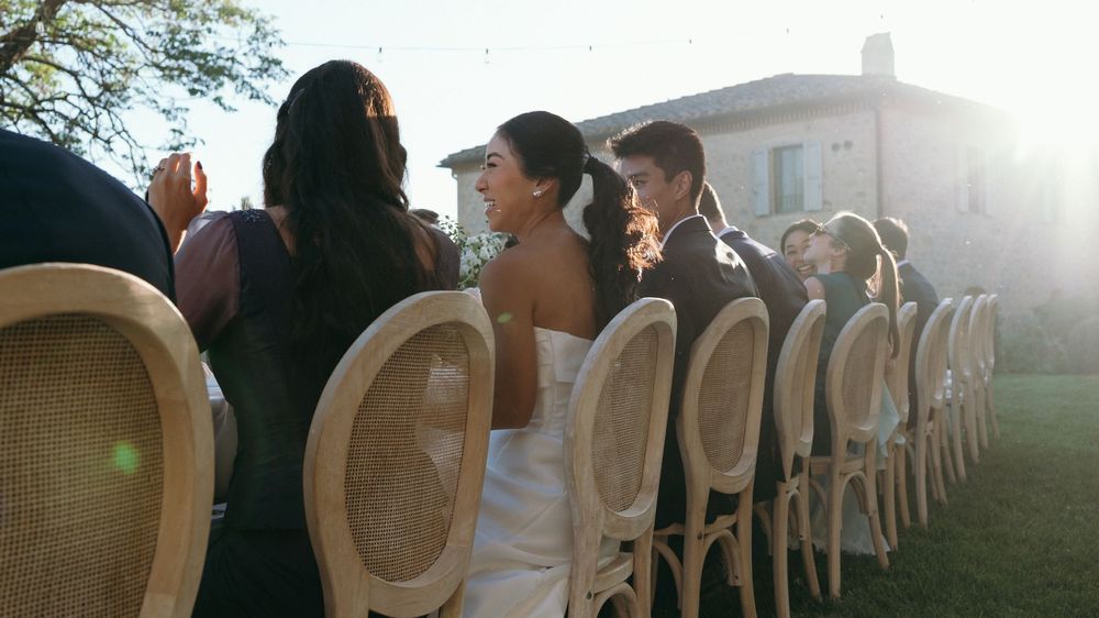 Bride and groom seated at outdoor wedding reception with woven rattan chairs in golden sunlight.