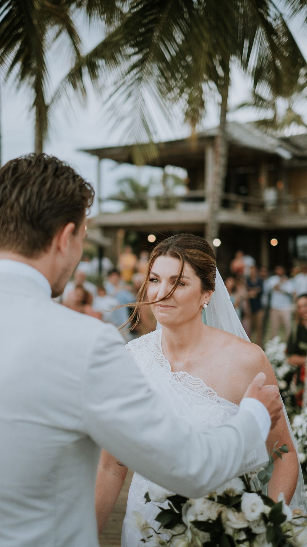 Groom gently brushing hair from bride's face during outdoor beach wedding ceremony.