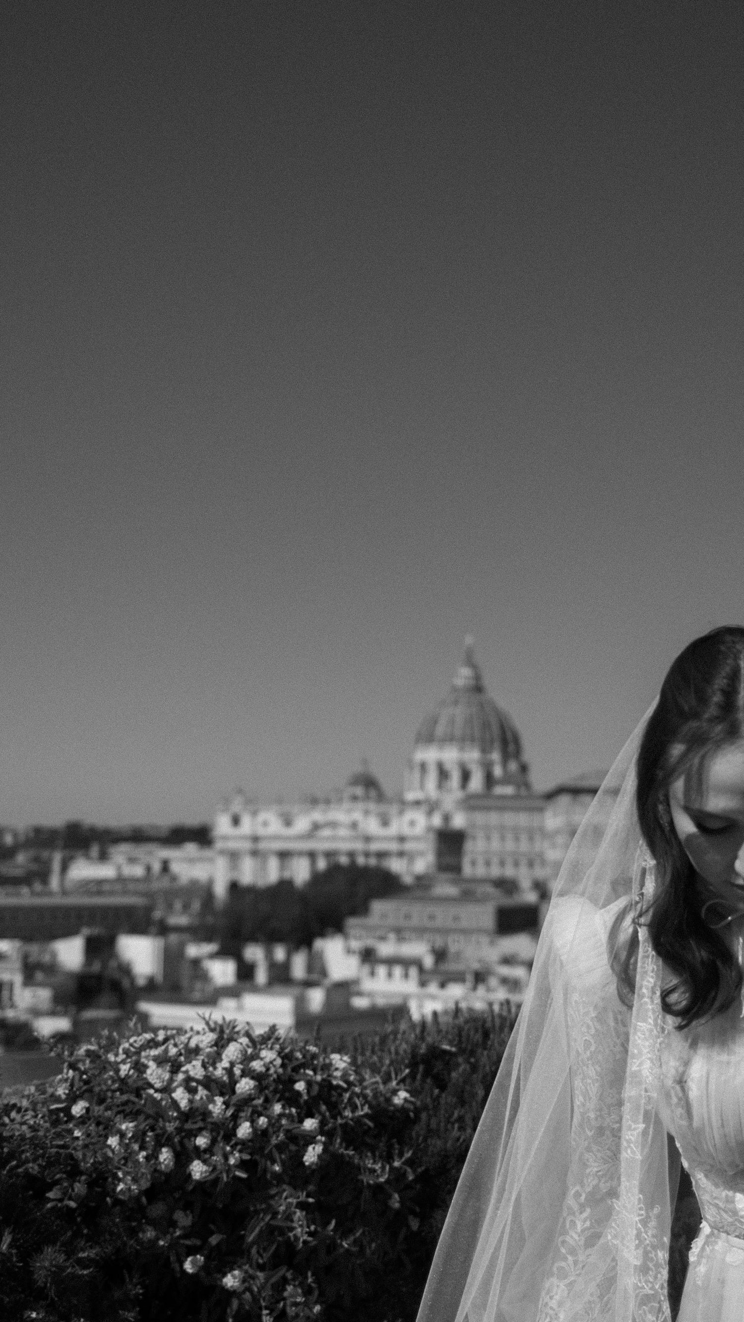 Black and white portrait of a bride in veil with St. Peters Basilica Rome skyline in the background.