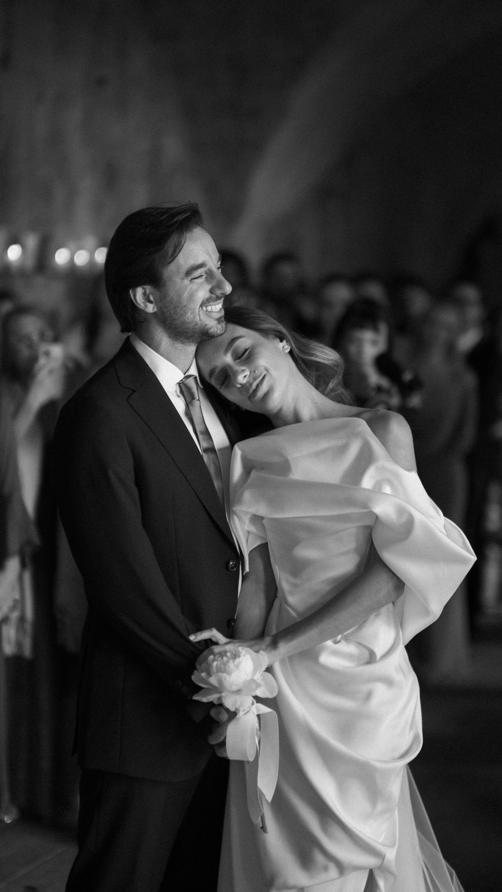 Black and white photo of joyful bride and groom embracing and laughing during wedding reception.