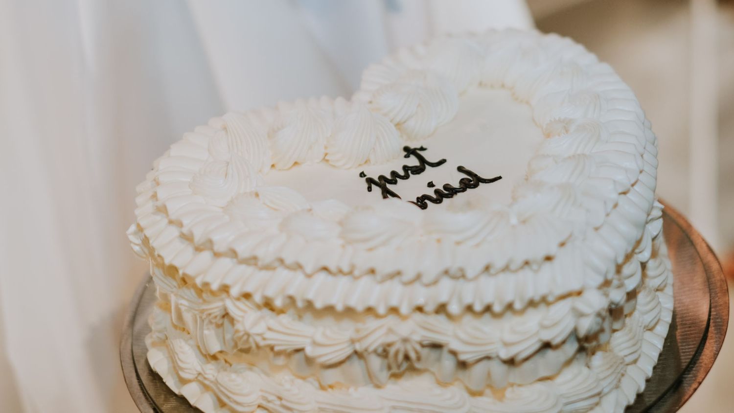 A vintage-style white wedding cake decorated with piped frosting and the words just wed.