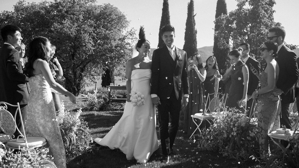 Black and white photo of bride and groom walking through confetti shower after outdoor ceremony.