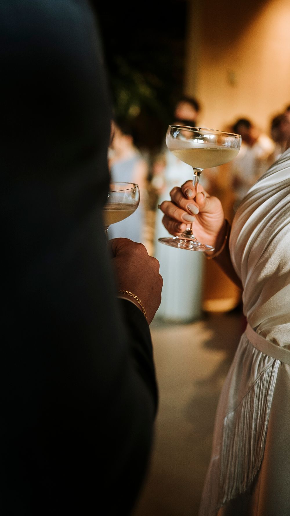 Close-up of bride and groom holding champagne coupe glasses at elegant wedding reception.