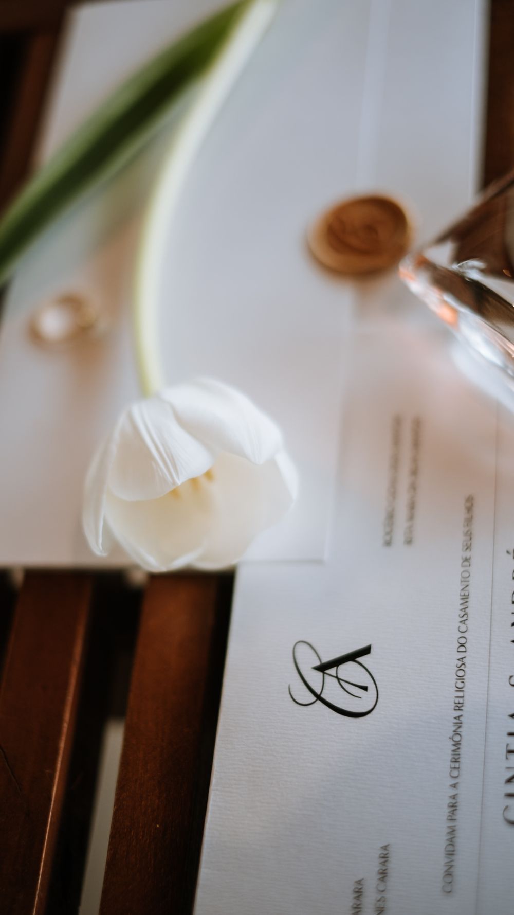 White tulip resting on elegant wedding invitation with wax seal and monogram detail.