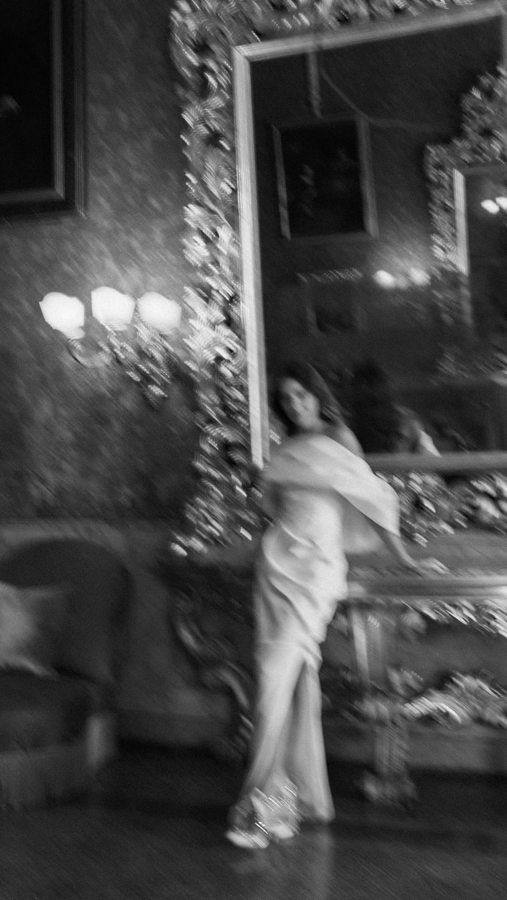Blurred black and white image of bride in white gown posing in an ornately decorated vintage interior.
