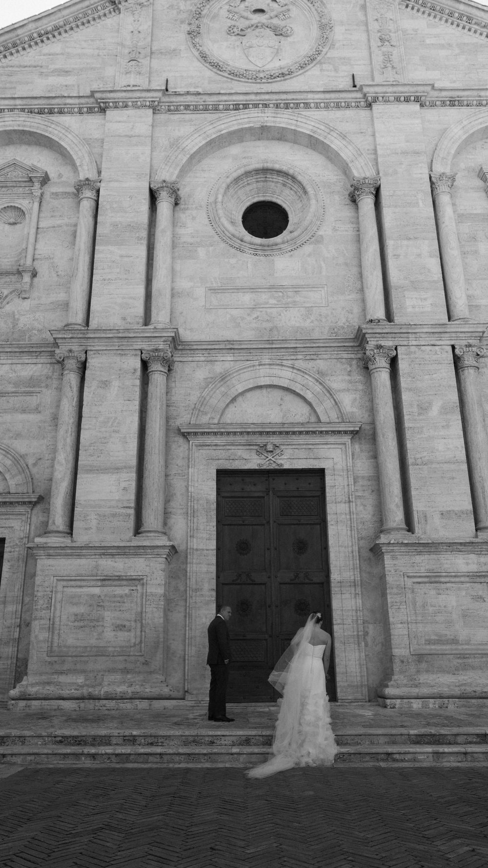 Black and white photo of a bride and groom standing before the ornate entrance of a historic Italian cathedral.