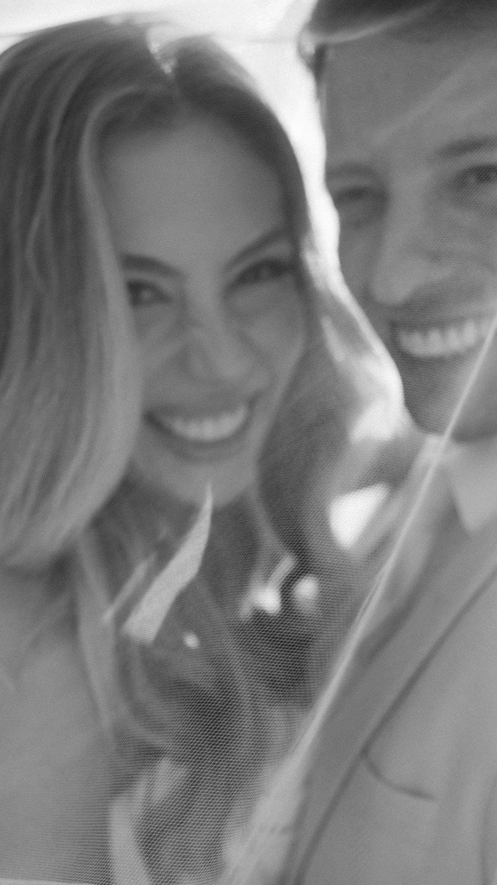 Smiling bride and groom pose together in a blurred black and white wedding portrait.