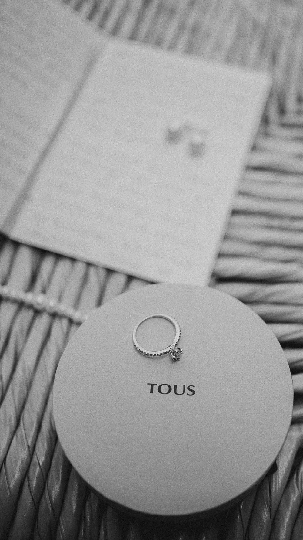Black and white close-up of diamond ring on TOUS jewelry box with earrings.