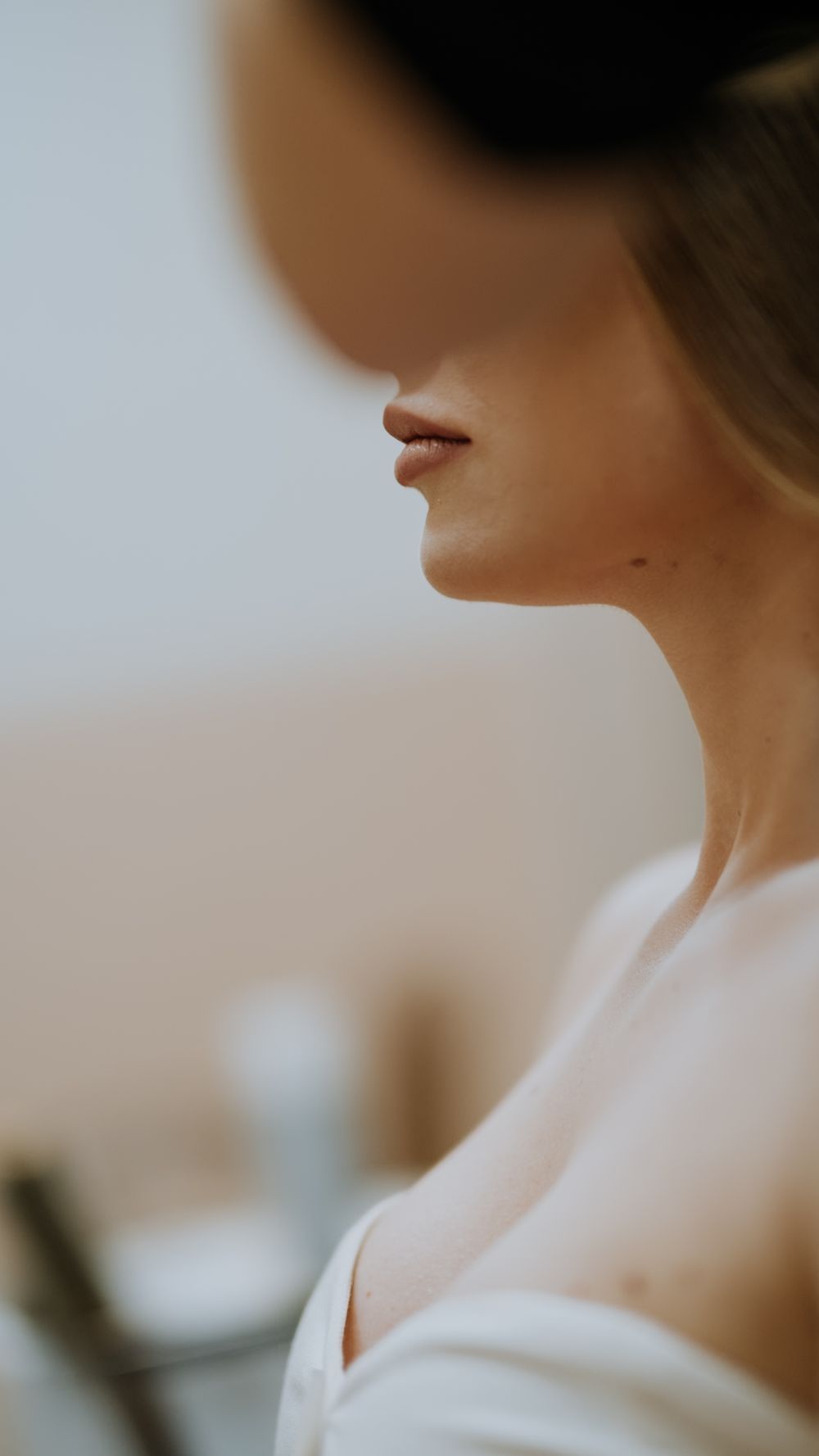 Close-up side profile of a bride with elegant updo hairstyle wearing a white off-shoulder dress during wedding preparations.