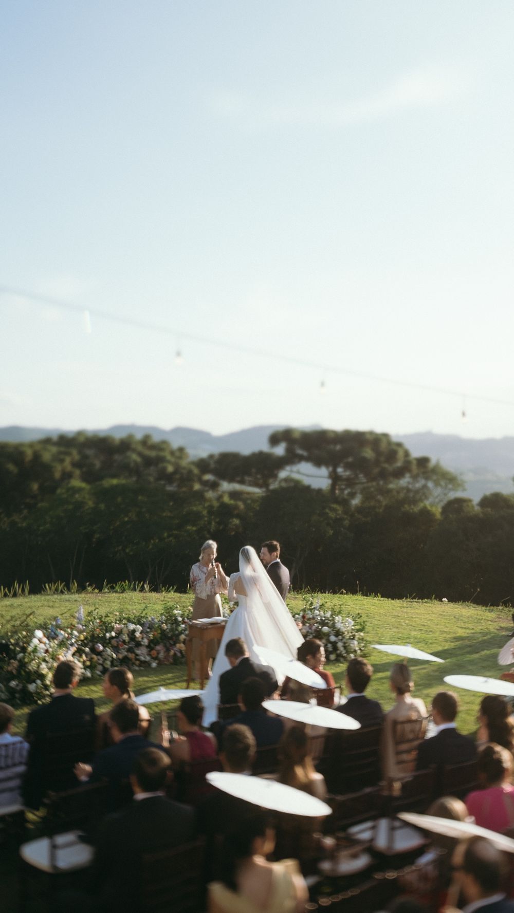 Bride and groom exchange vows at outdoor hilltop ceremony with panoramic mountain views and guests.