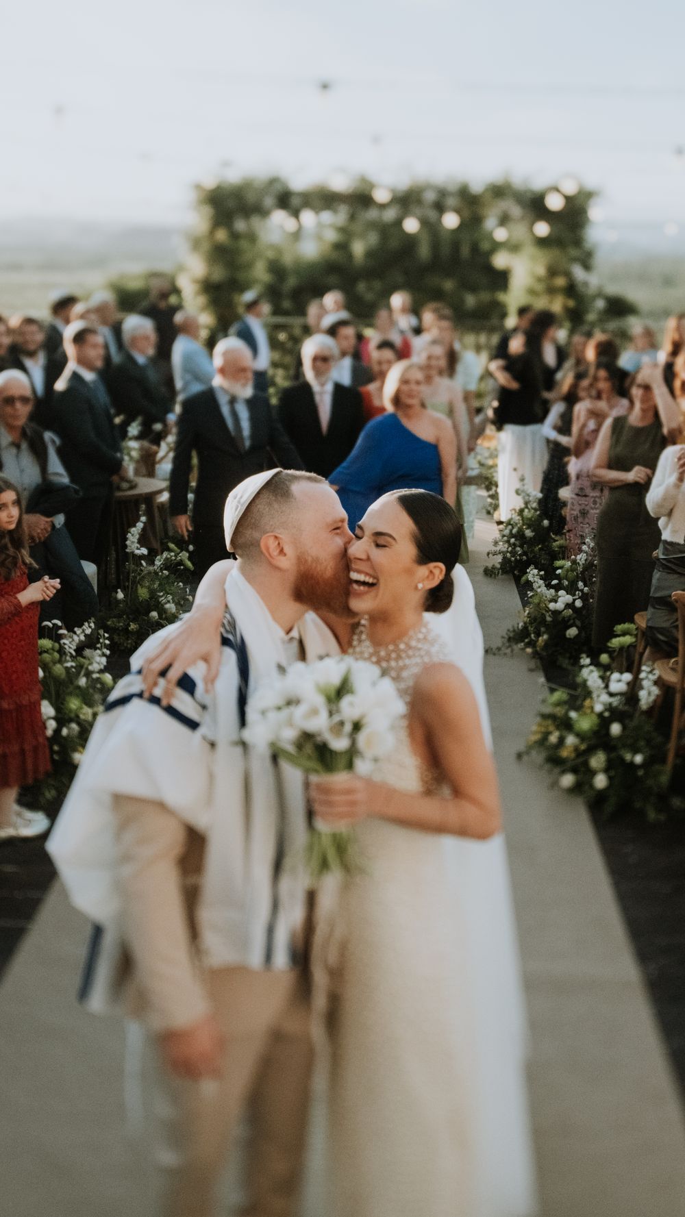 Joyful newlyweds walk down the aisle as guests celebrate at an outdoor garden wedding.