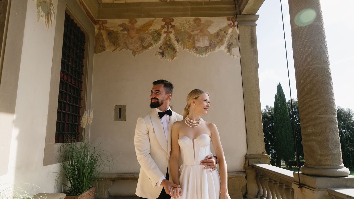 Elegant bride and groom posing under ornate frescoed archway at Italian villa wedding.