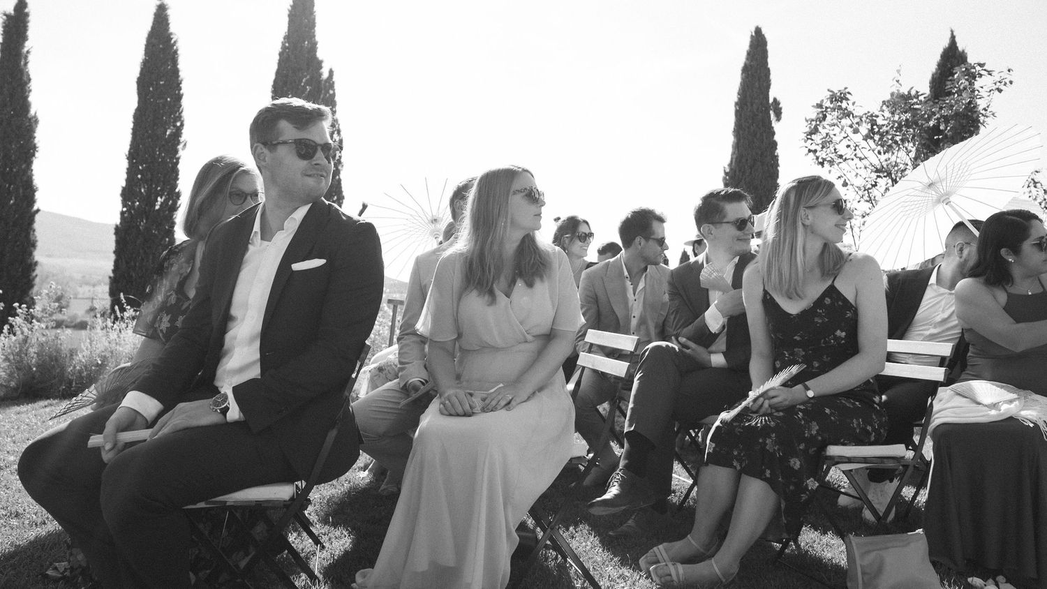 Black and white photo of wedding guests seated outdoors at a ceremony.