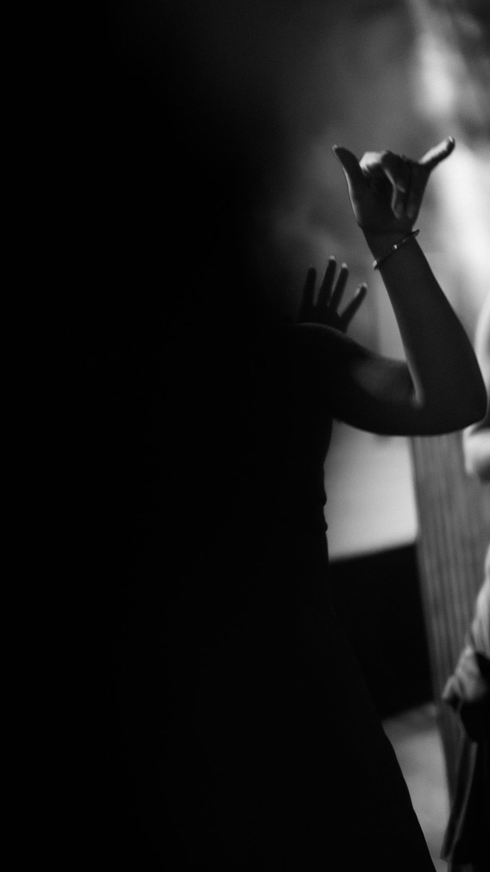 Dramatic black and white silhouette of a person raising their hands during a wedding celebration.