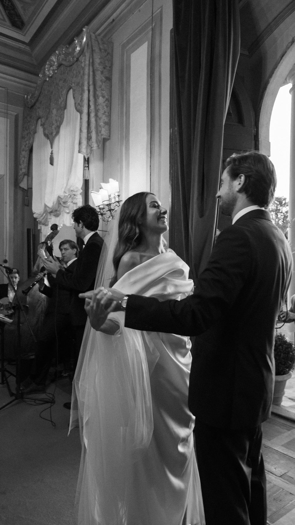 Black and white photo of bride and groom sharing first dance with live band performing in elegant ballroom.