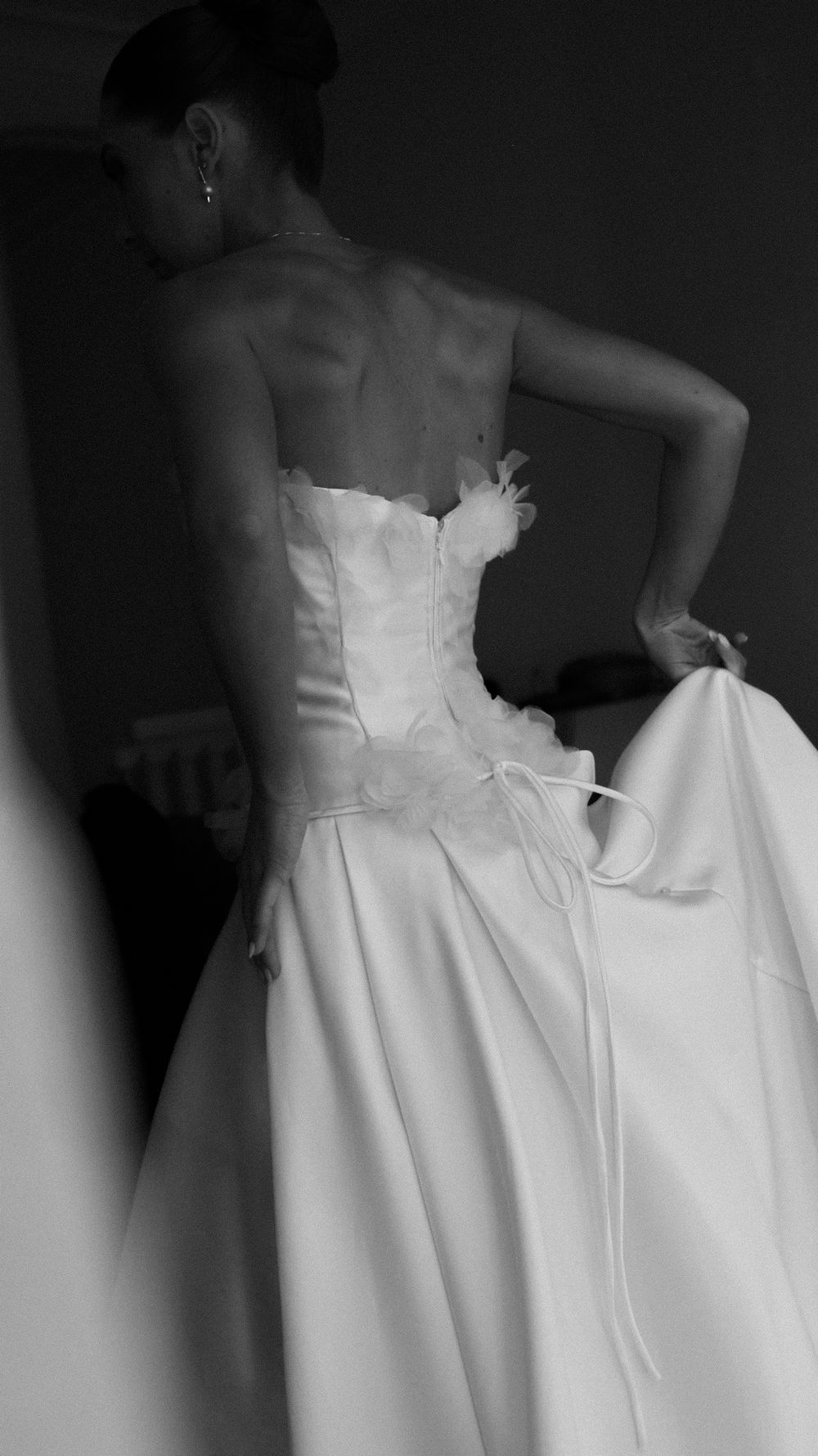 Black and white photo of a bride in a strapless corset wedding gown viewed from behind in dim lighting.