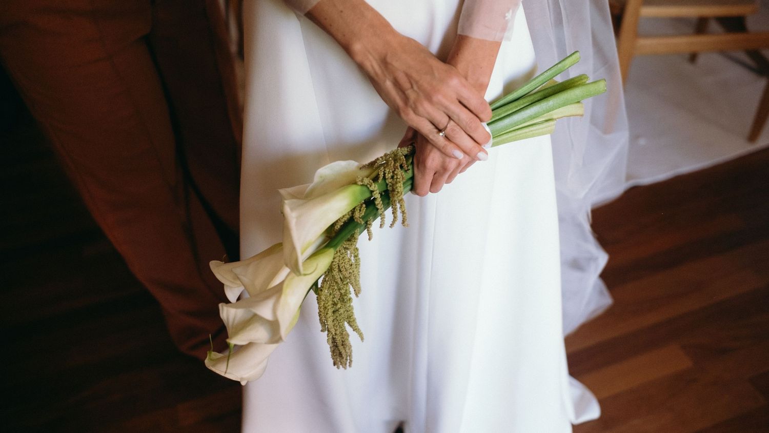 Close-up of bride holding minimalist green calla lily bouquet in white wedding dress.