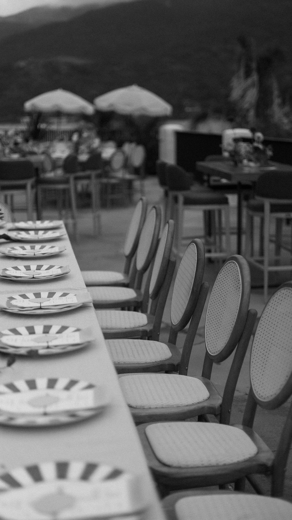Elegant outdoor wedding reception table set with decorative plates and classic cane-back chairs by the waterfront.