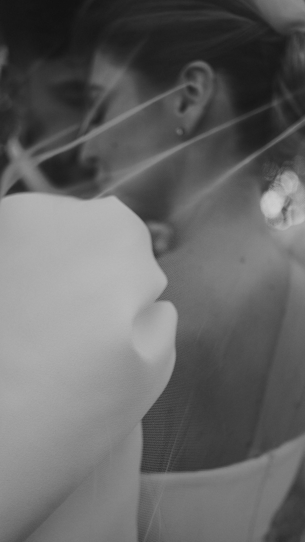 Close-up black and white photo of a bride with veil strings across her face.