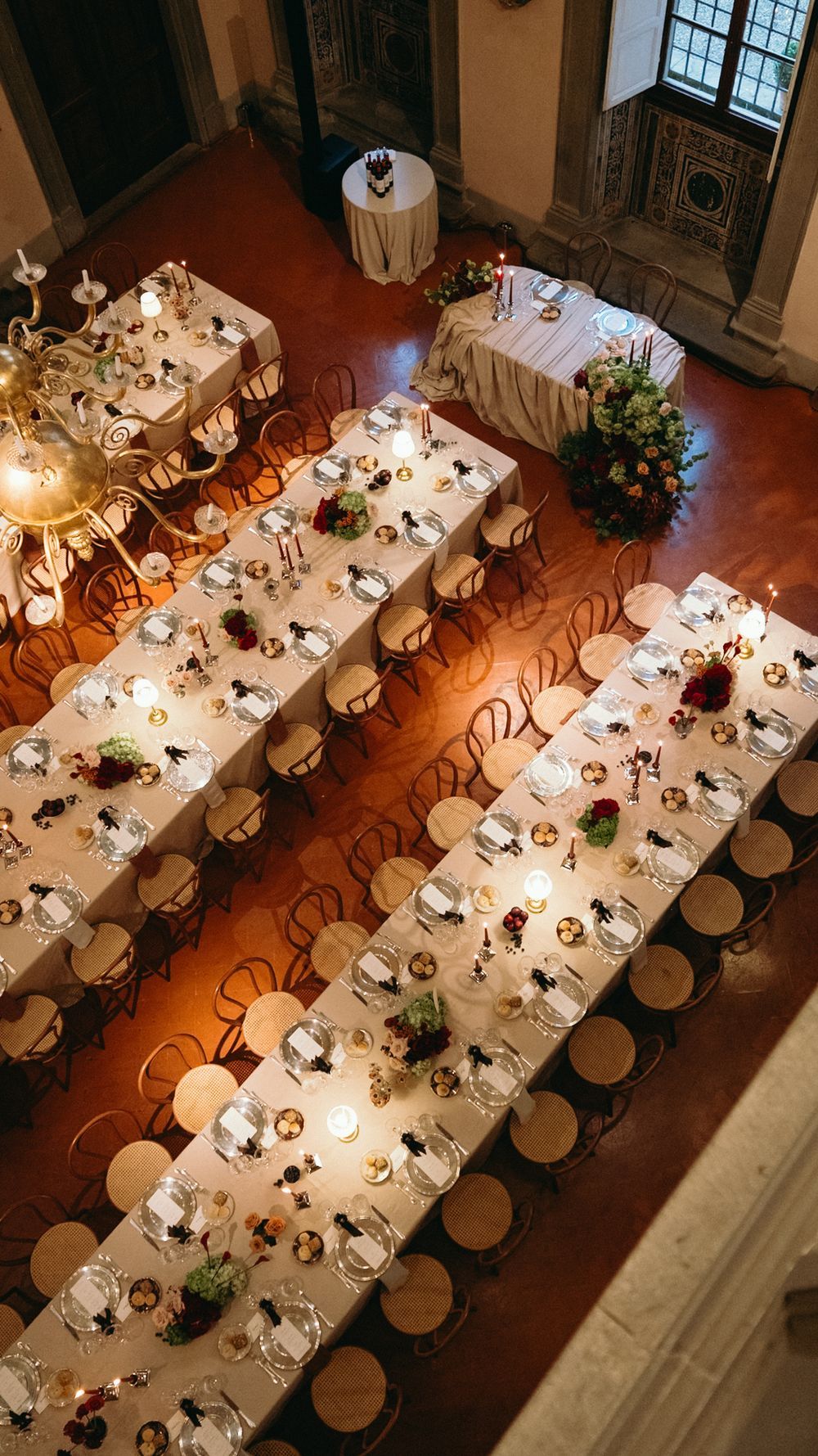 Aerial view of elegantly set wedding reception tables with candles, floral centerpieces, and bentwood chairs in a grand hall.