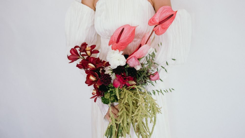 Bride holding a stunning cascading bouquet with pink anthuriums, deep red orchids, and trailing greenery.