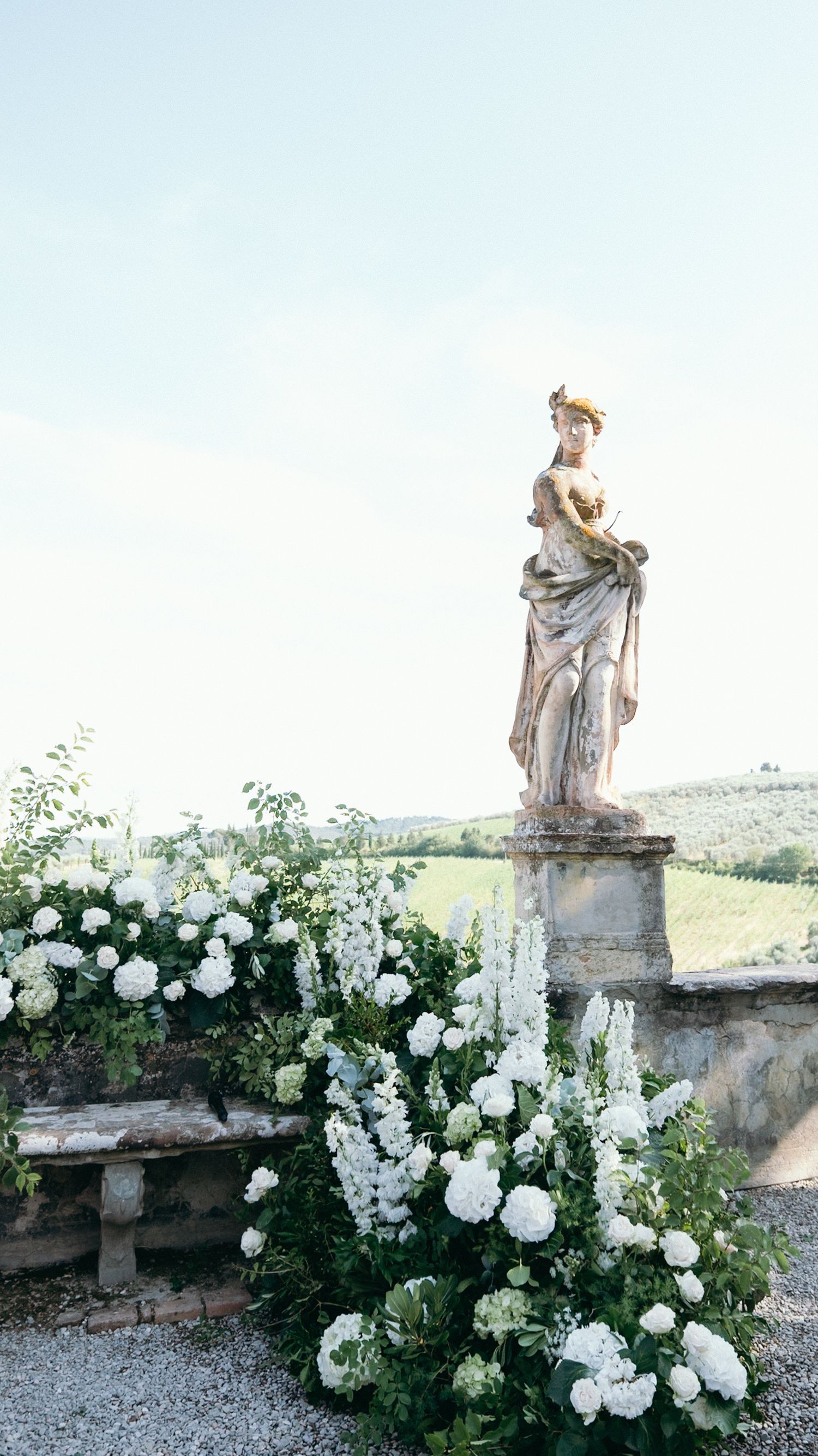 Classical stone statue surrounded by abundant white hydrangeas and greenery at an elegant Tuscan wedding ceremony.
