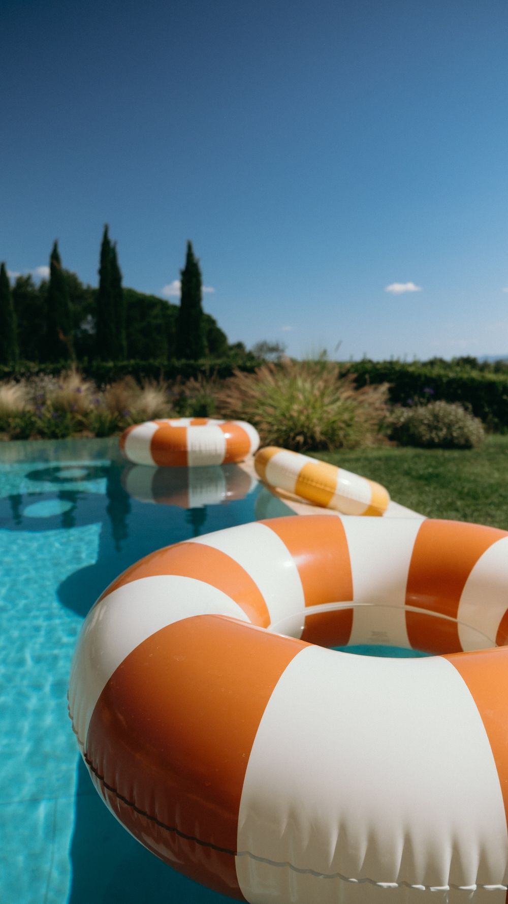Close-up of orange and white striped inflatable pool rings floating in a clear blue outdoor swimming pool.