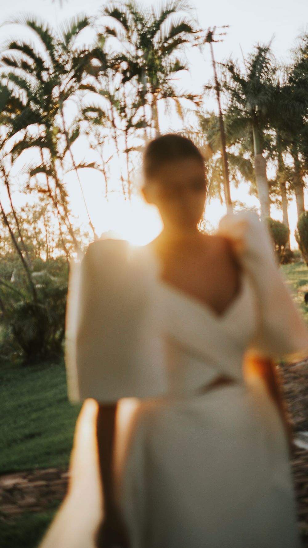 Blurred artistic shot of bride in white gown at sunset surrounded by palm trees.