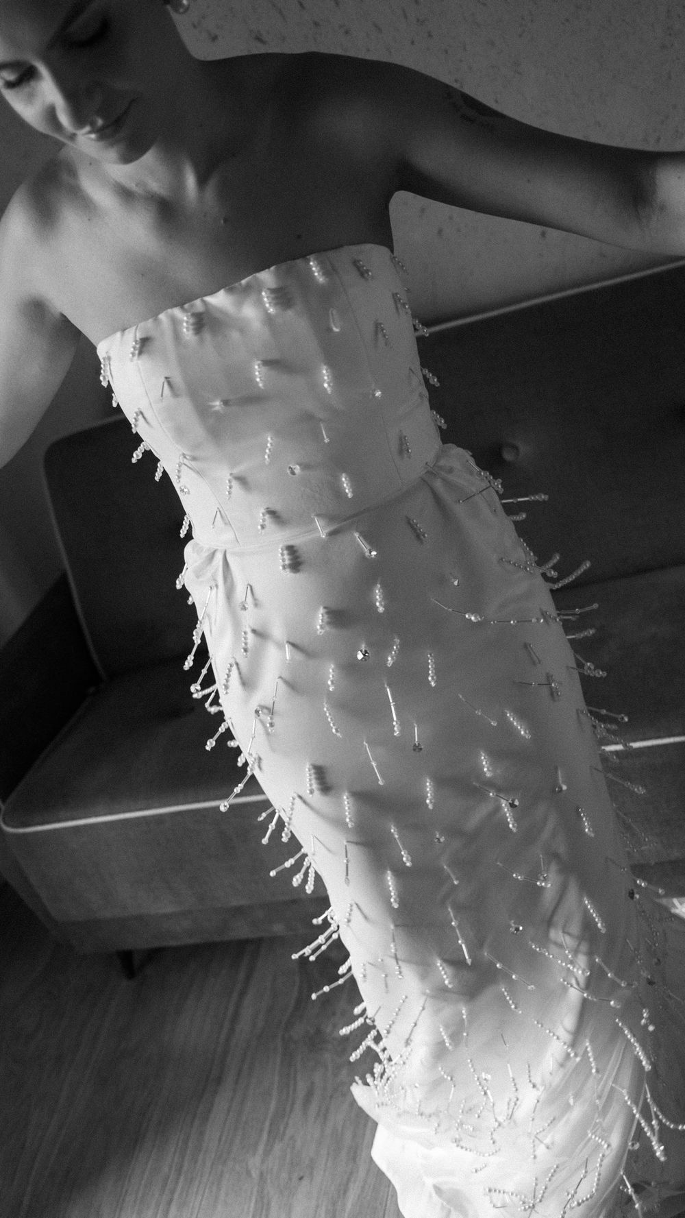 Black and white photo of bride in strapless beaded fringe wedding dress posing indoors.