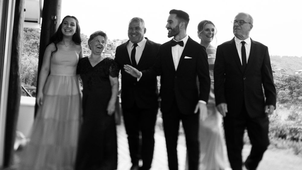 Black and white photo of groom walking with family members at wedding venue.