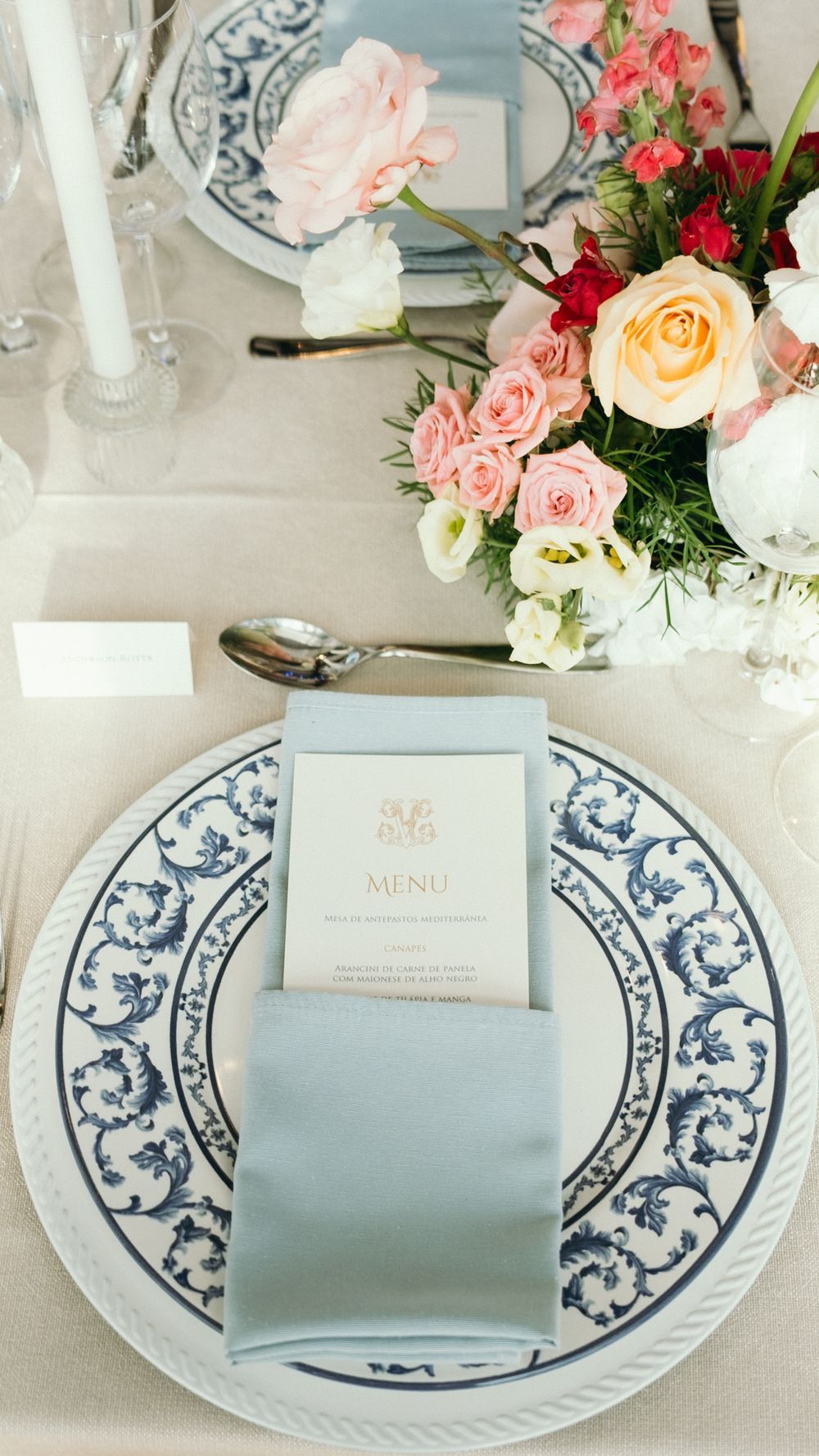 Elegant wedding table setting with blue floral china, grey napkin, menu card, and pink roses.
