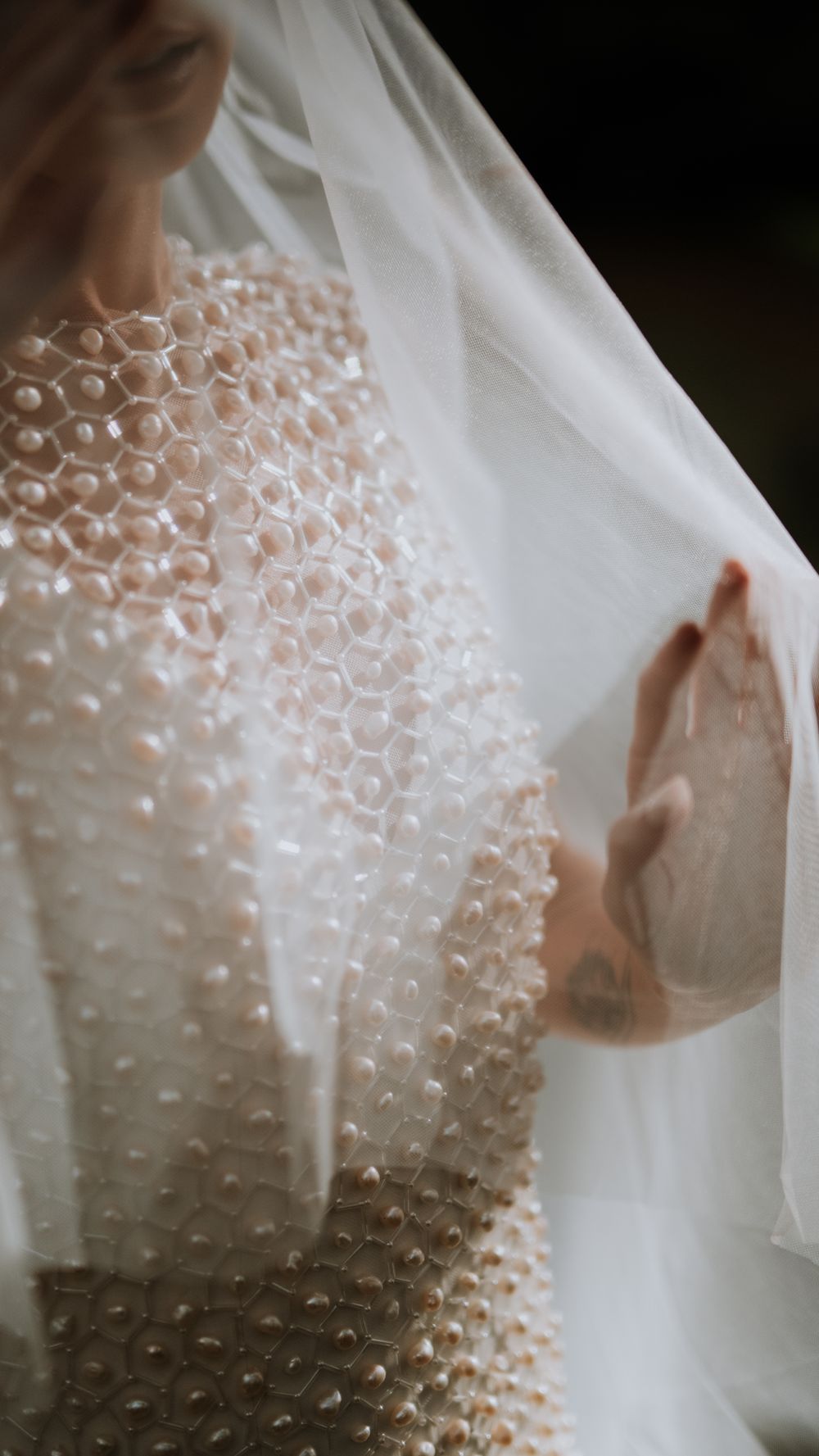 Close-up of a pearl-embellished wedding gown with sheer veil draped over the bride.