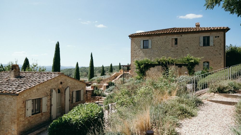 Rustic Tuscan stone villa surrounded by cypress trees and Mediterranean garden landscape.