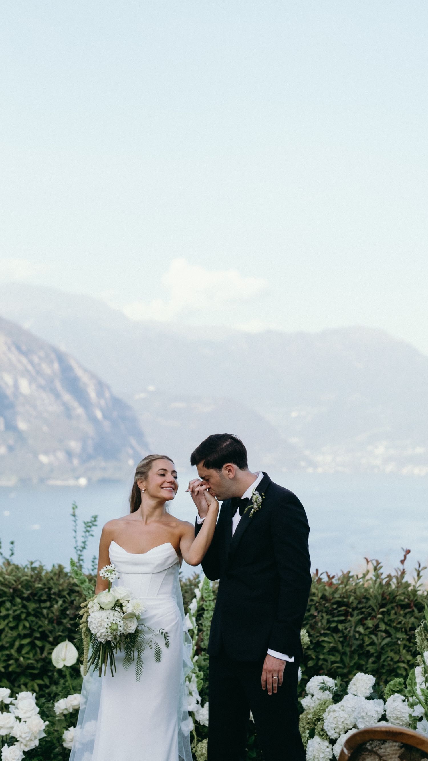 Bride and groom share a romantic moment with stunning Lake Como mountain backdrop behind them.
