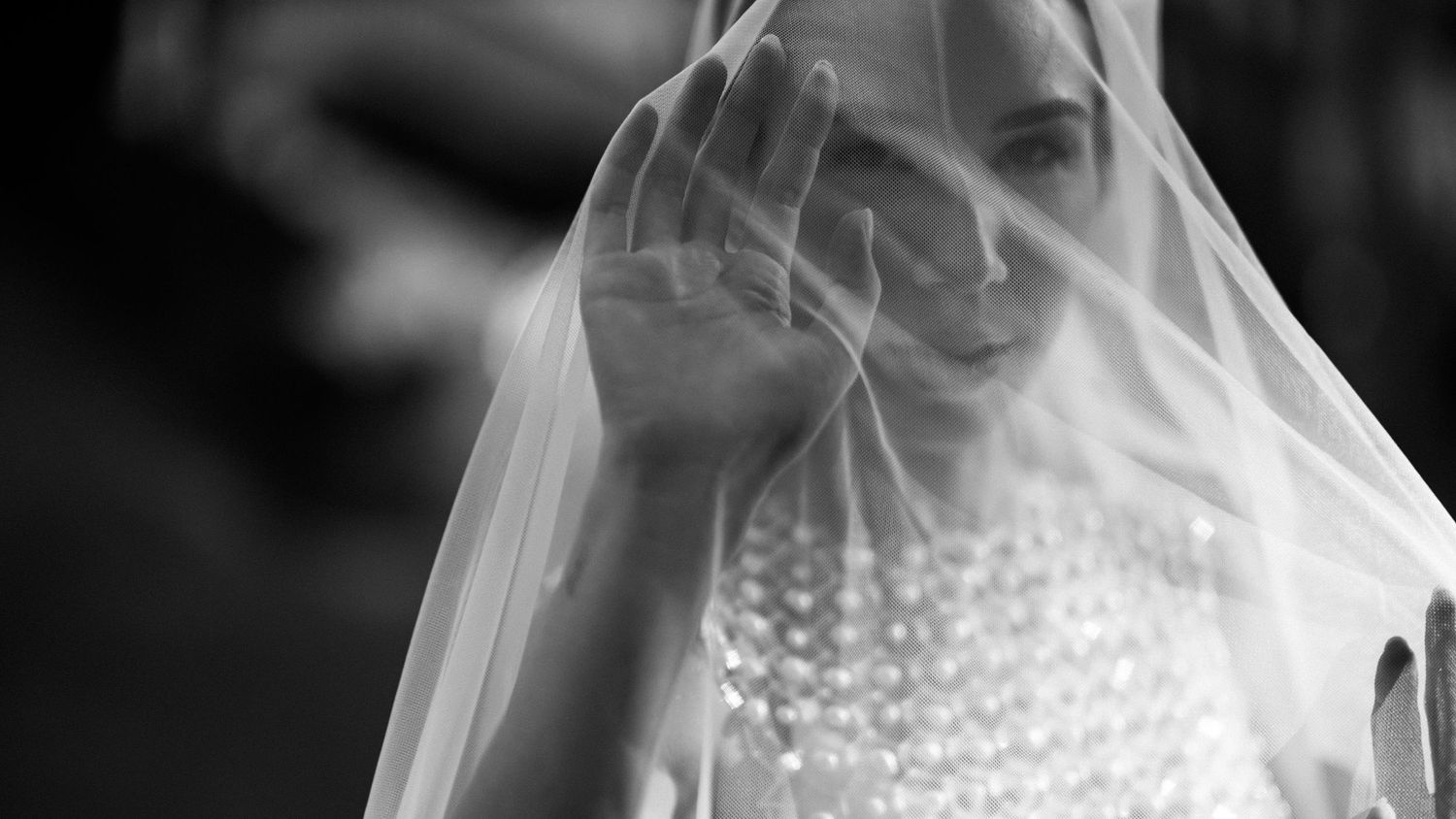 Black and white close-up of smiling bride lifting delicate wedding veil over her face.
