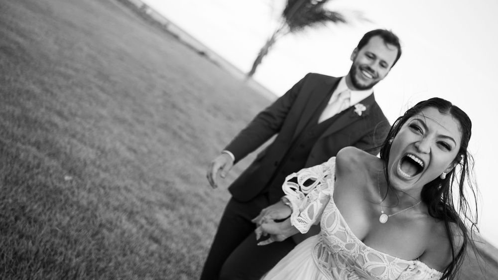 Joyful bride and groom laughing outdoors in black and white wedding portrait with coastal backdrop.