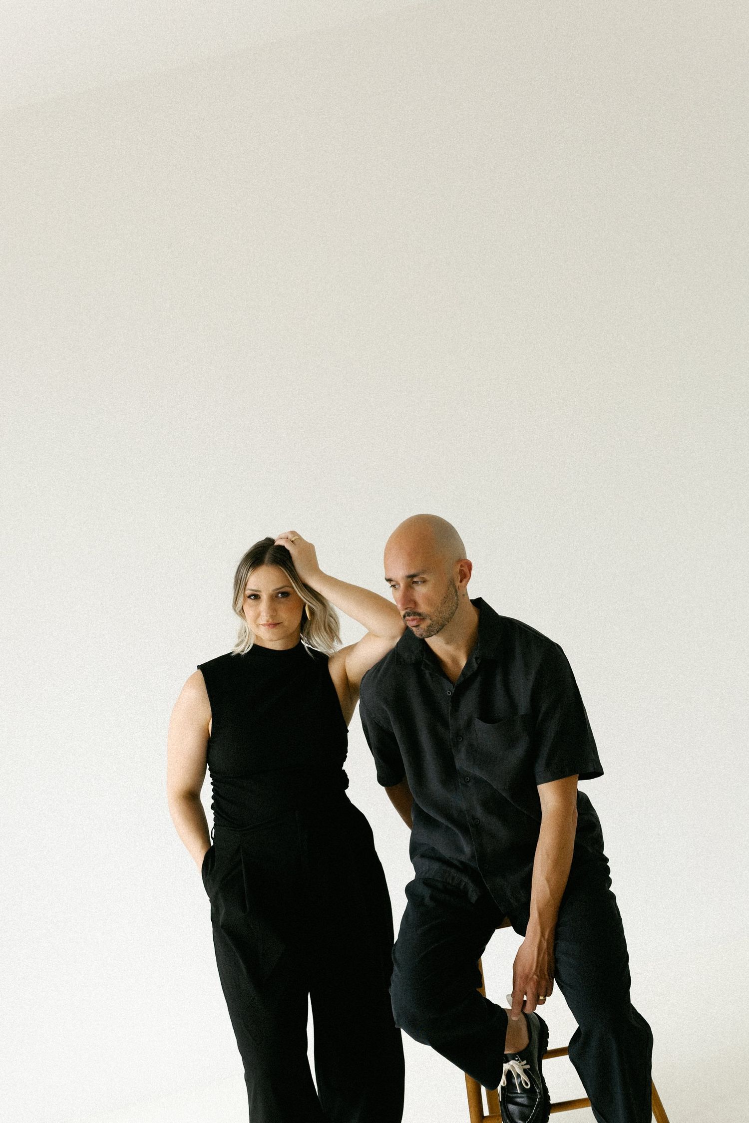 Two photographers dressed in black posing in a bright minimalist studio space.