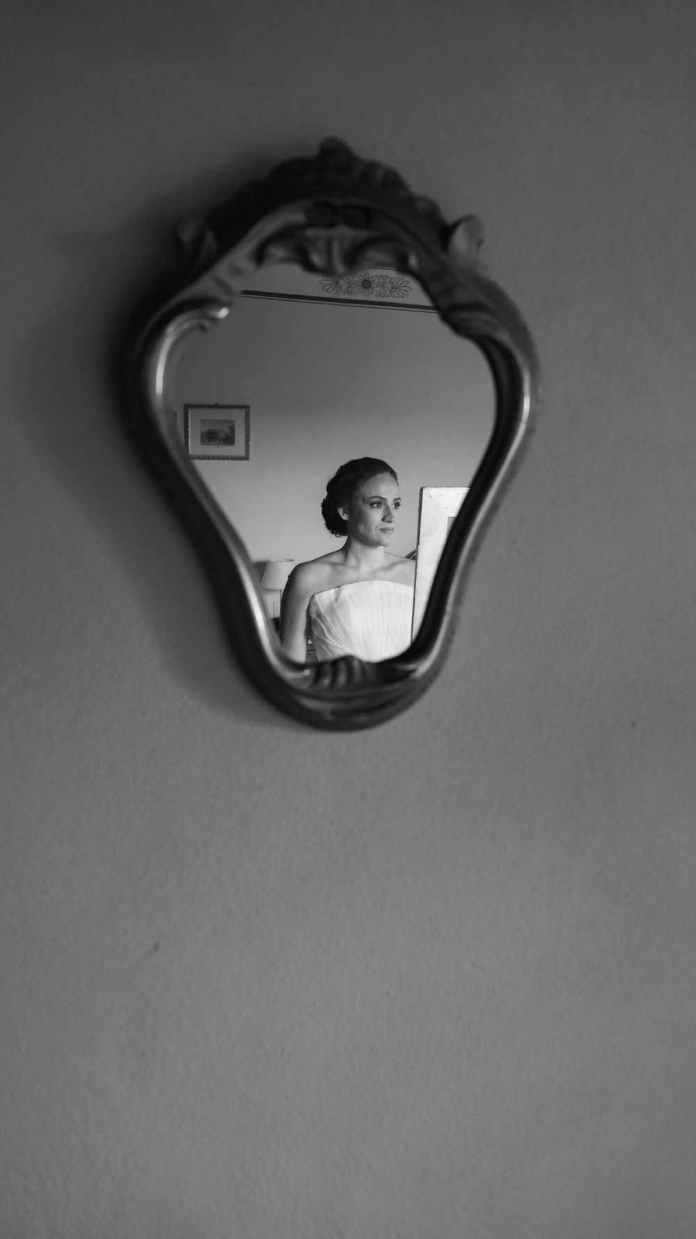Black and white reflection of a bride in an ornate vintage mirror on a plain wall.