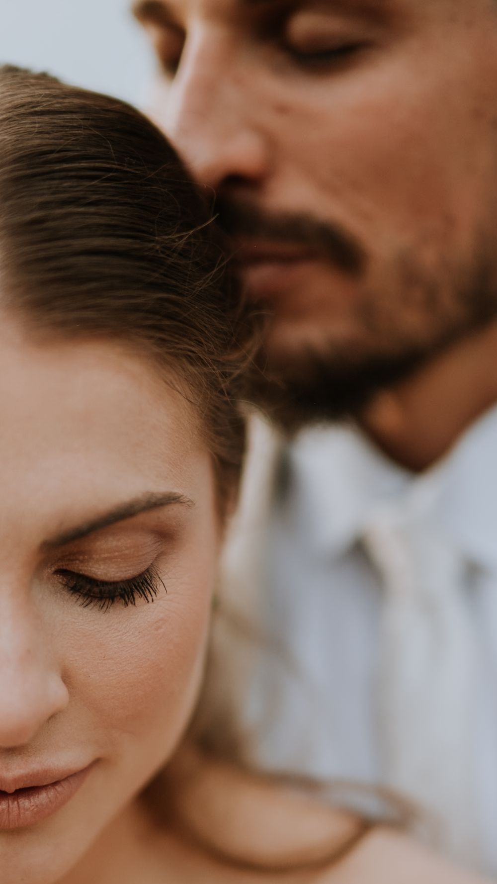 Intimate close-up of a groom tenderly kissing his bride on the head during their wedding day portrait session.