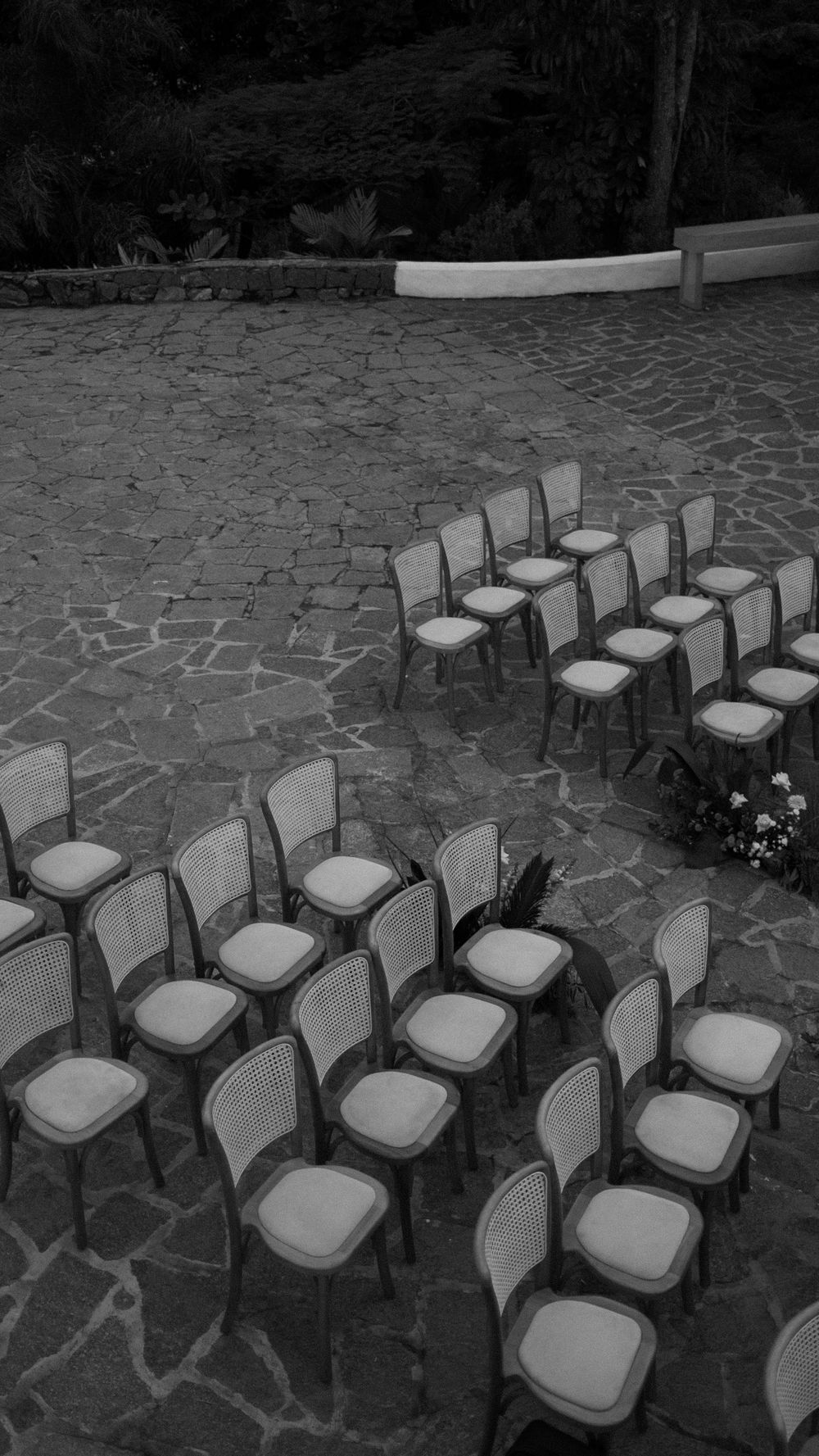 Black and white aerial view of rows of cane-back chairs arranged on cobblestone for an outdoor wedding ceremony.