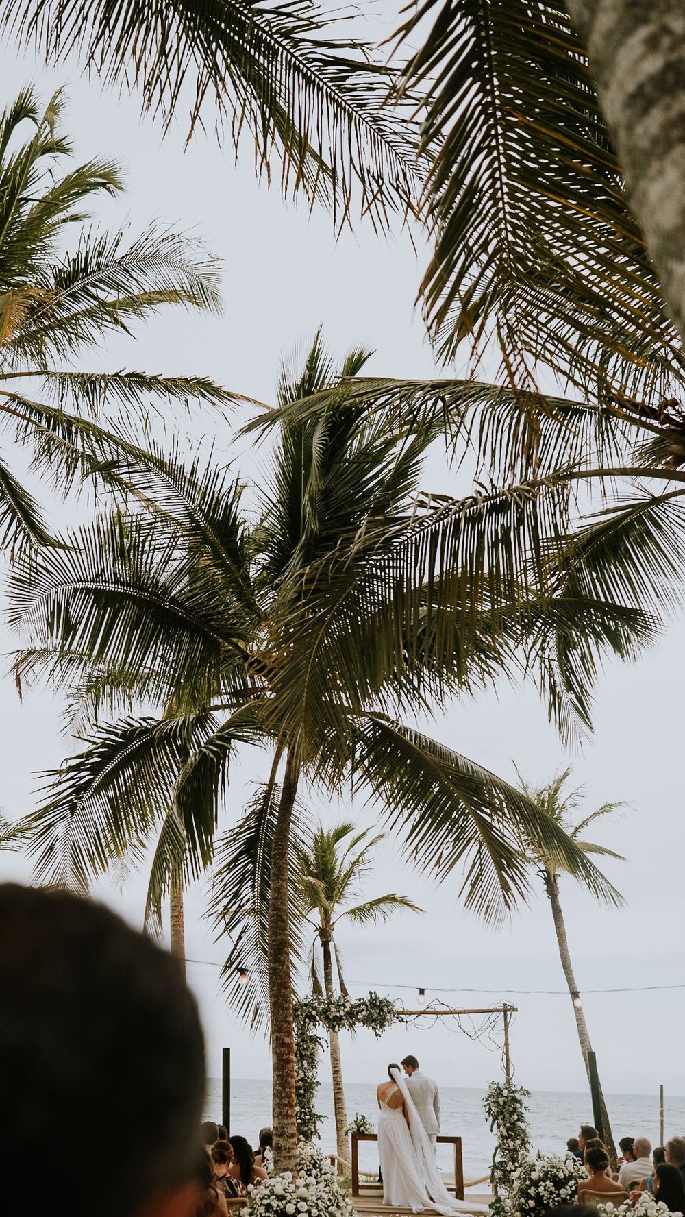 Bride and groom at altar beneath swaying palm trees during tropical beach wedding.