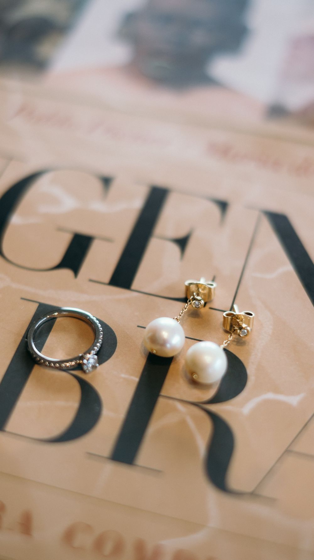 Close-up of pearl drop earrings and diamond ring resting on fashion magazine pages.