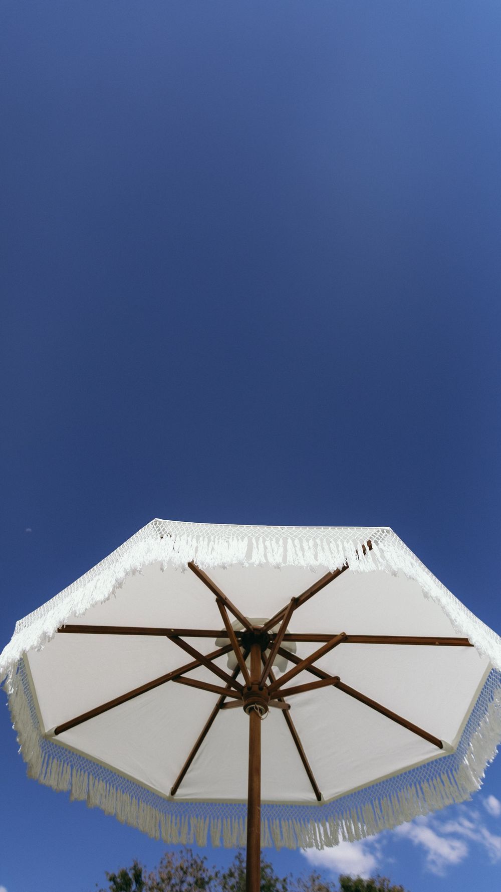 Low angle view of white fringed patio umbrella against a clear bright blue sky.