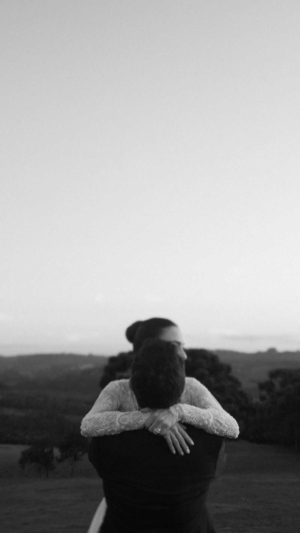 Couple embracing at sunset with scenic hills in black and white wedding photography.