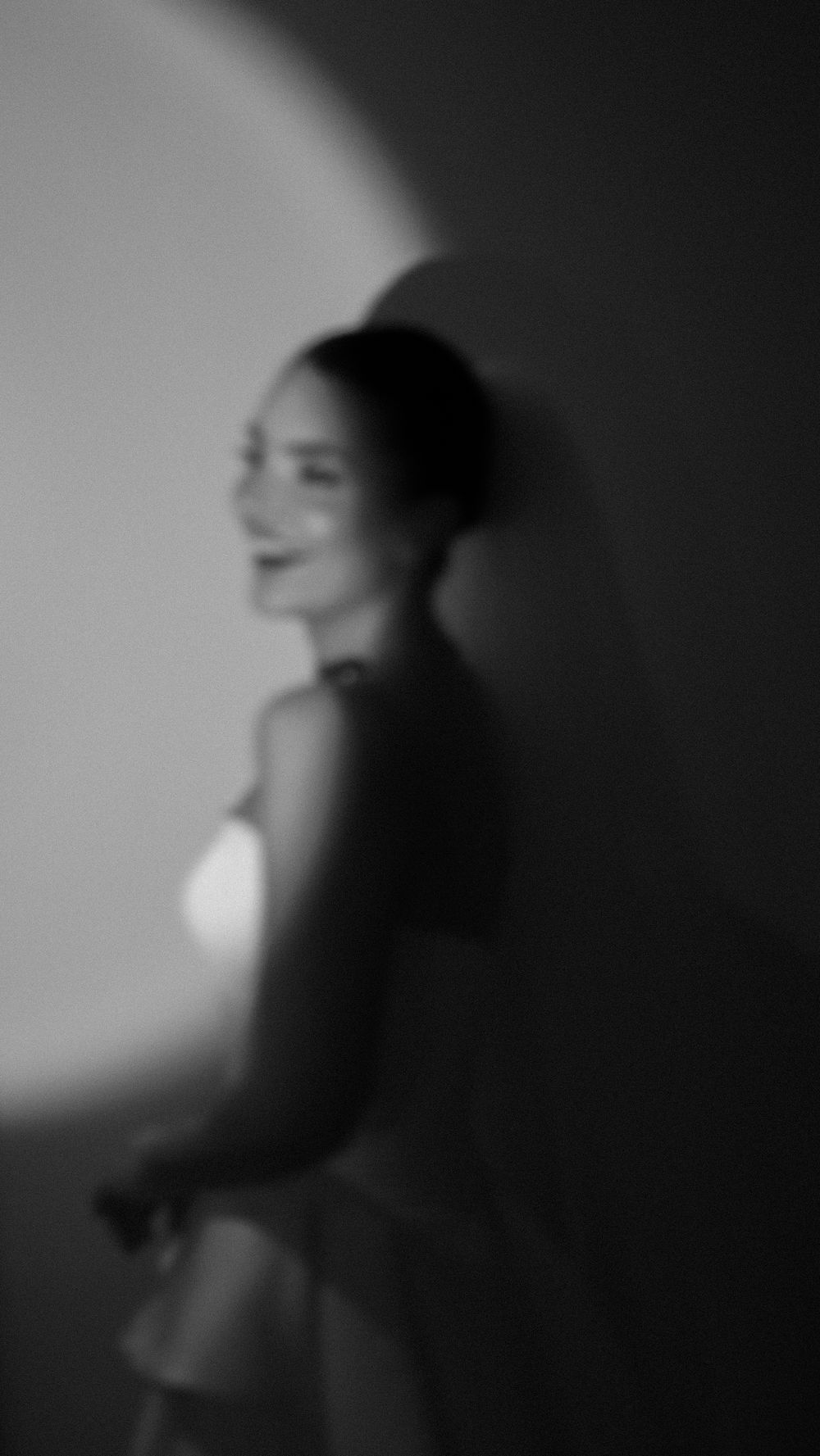 Blurry black and white portrait of a smiling woman with a dramatic circular light behind her.