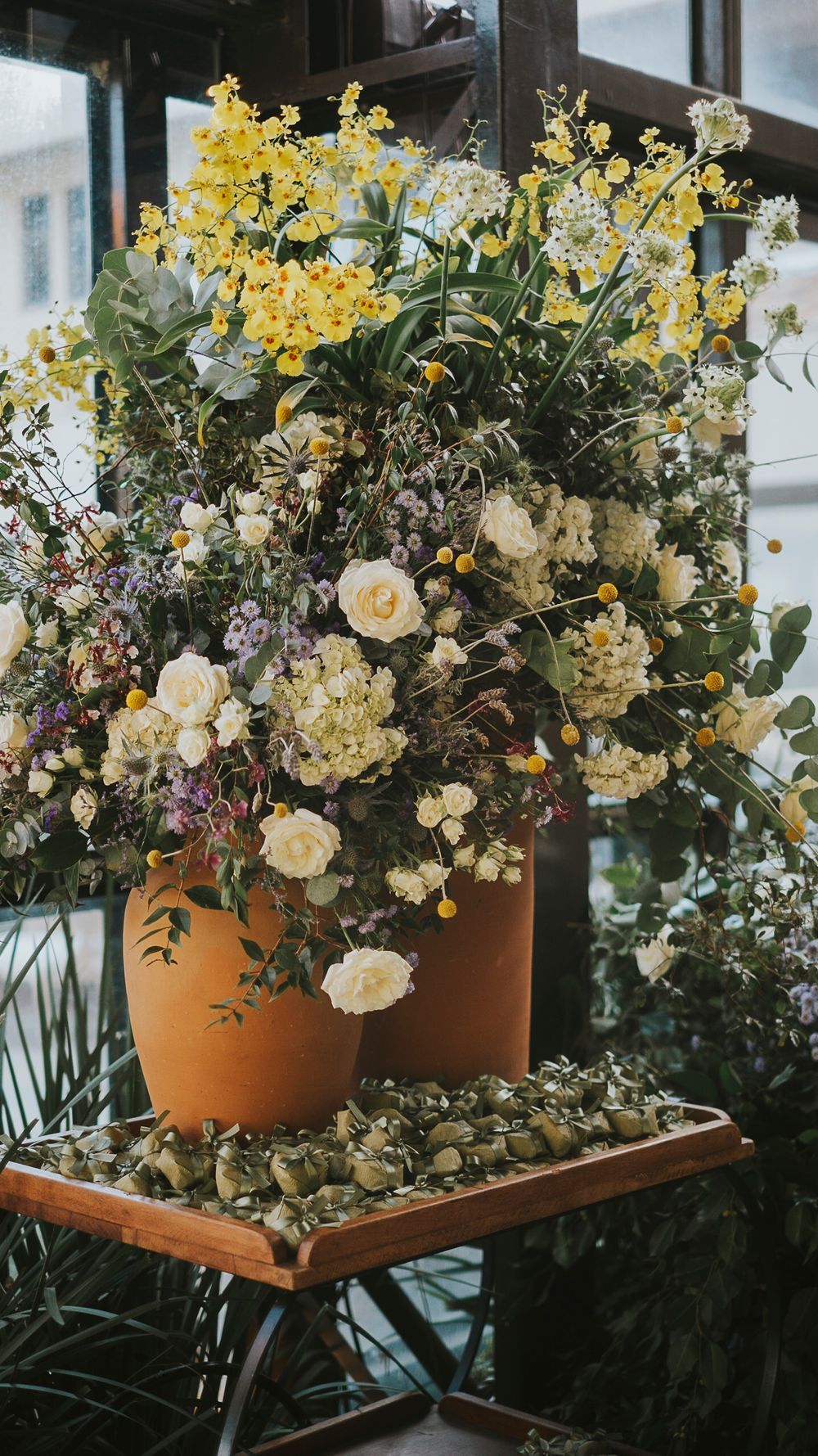 Lush floral arrangement with yellow, white, and purple blooms in terracotta vases at wedding venue.