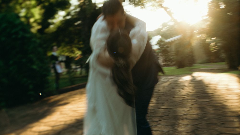 Blurred romantic photo of bride and groom kissing on sunlit garden pathway.
