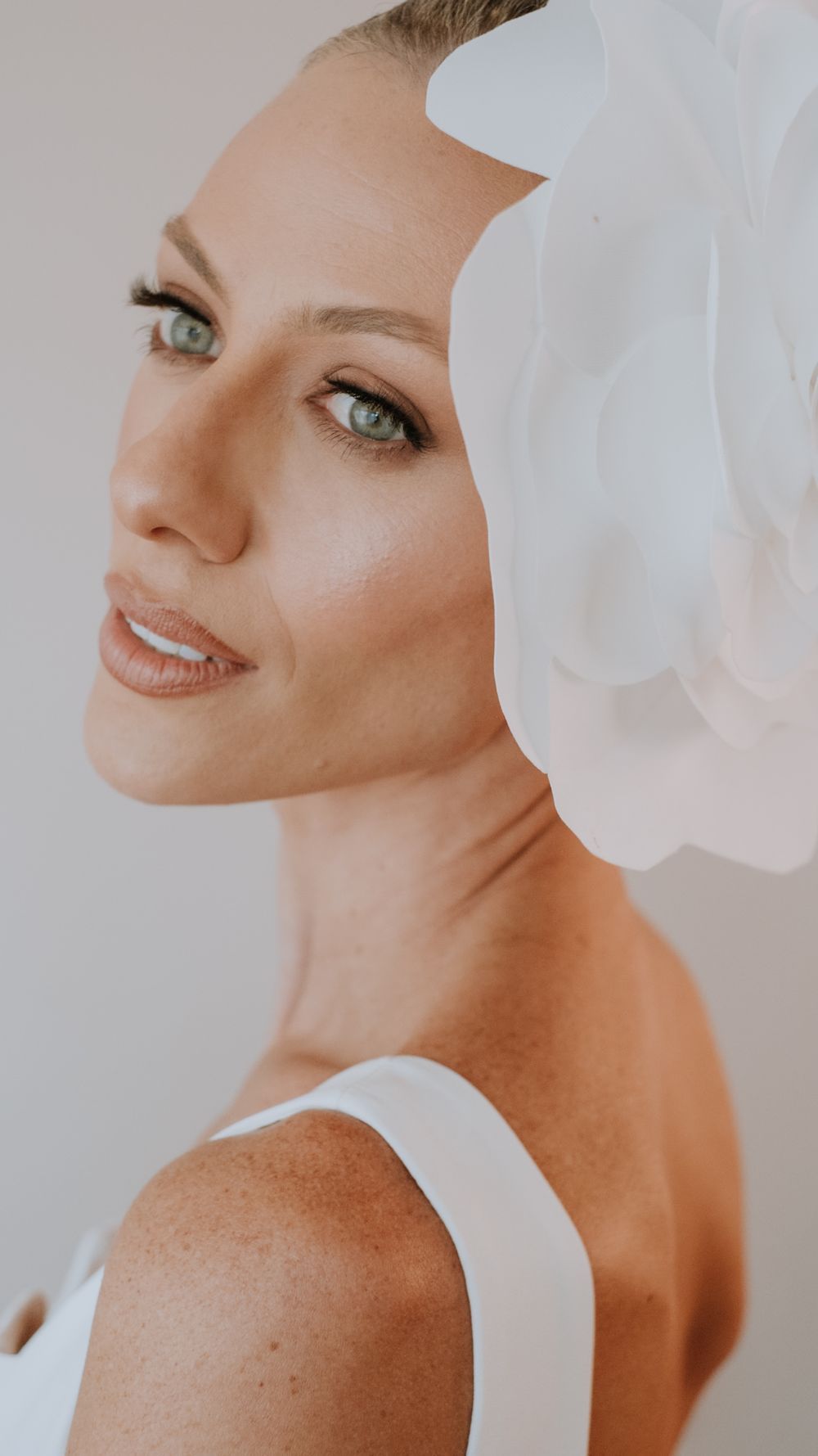 Close-up portrait of elegant bride with blue eyes wearing white floral hair accessory and white gown.