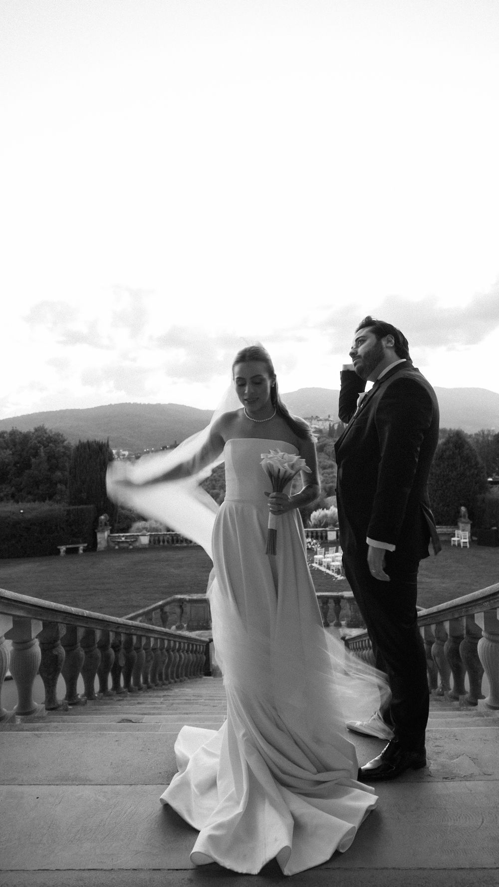Black and white photo of bride and groom on terrace with scenic landscape behind.